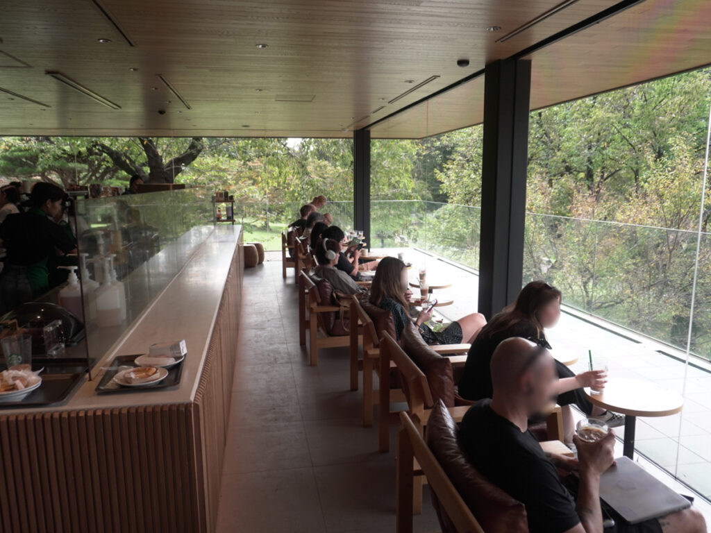 新宿御苑スターバックス。左にバーカウンター、右に窓際ソファ列。ガラス越しに緑が見える。