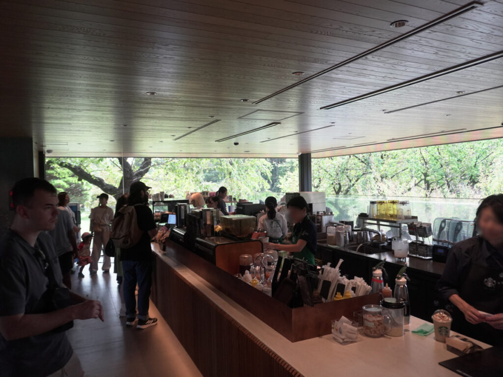 窓際のソファ席の列。小さめの丸テーブルが並び、外に庭園の緑が広がる。