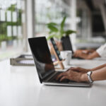 自然光の入るデスクでパソコン作業をする人物（バーチャルオフィスの使用イメージ）