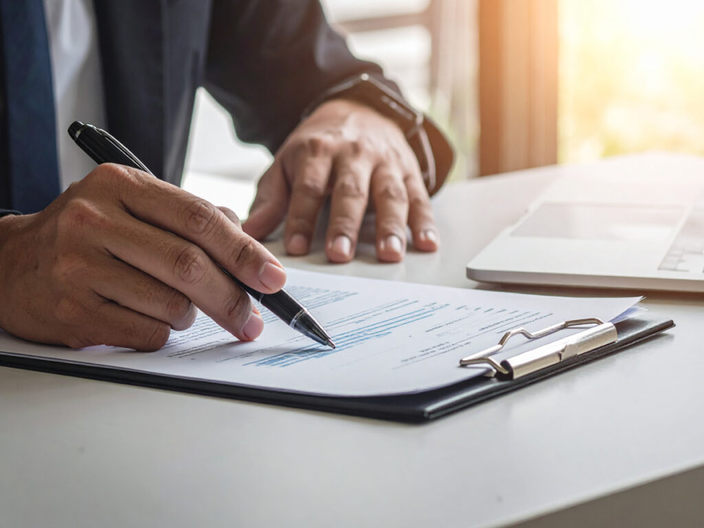 登記申請書類にサインする手元(契約書・クリップボード・PC)