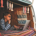 キャンピングカーの中でノートPCを操作しながらワーケーションするノマドワーカー