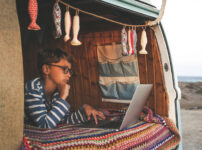 キャンピングカーの中でノートPCを操作しながらワーケーションするノマドワーカー