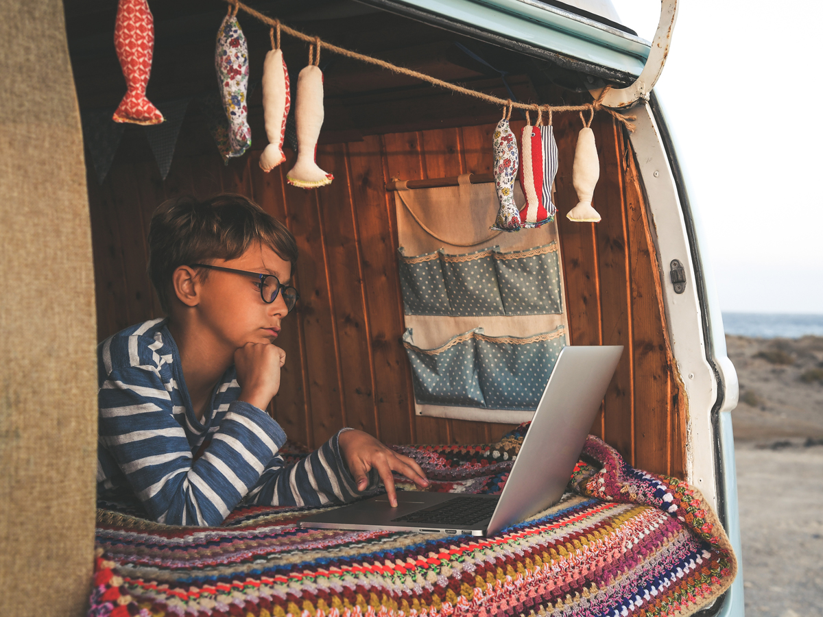 キャンピングカーの中でノートPCを操作しながらワーケーションするノマドワーカー
