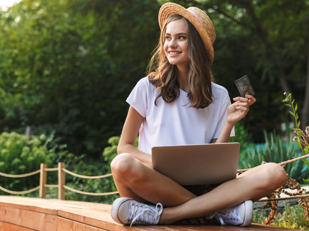 森の中でノートPCを開き、クレジットカードを手にオンライン決済をする女性ノマドワーカー