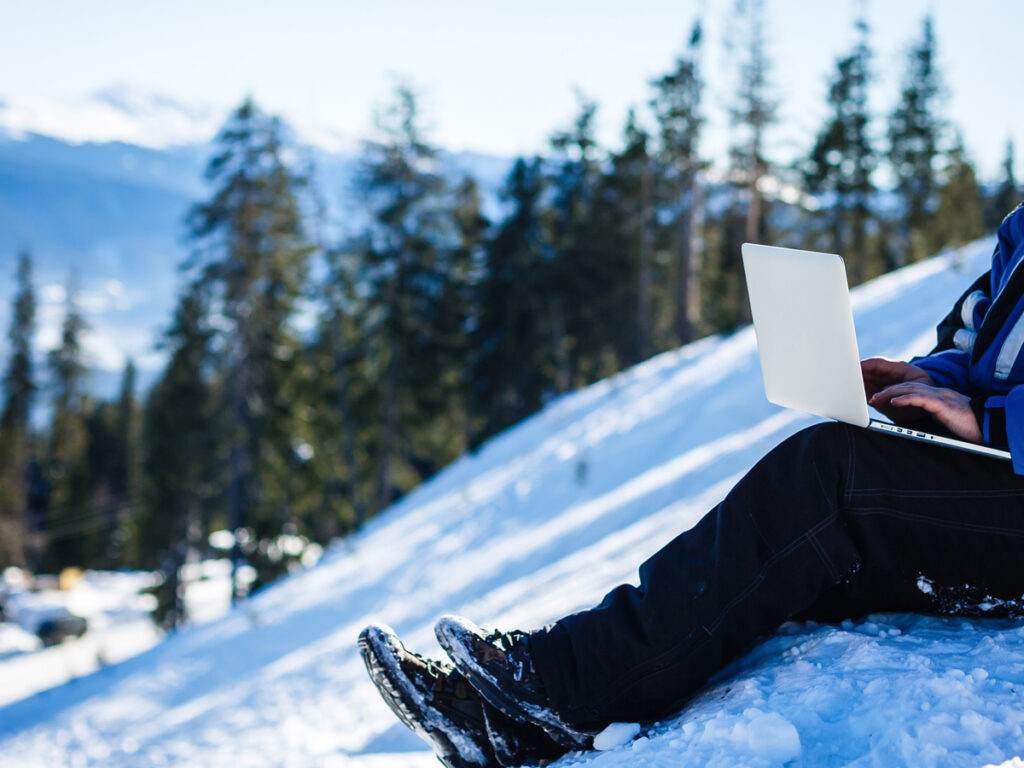 雪山のゲレンデでノートPCを操作するアウトドアスタイルのノマドワーカー