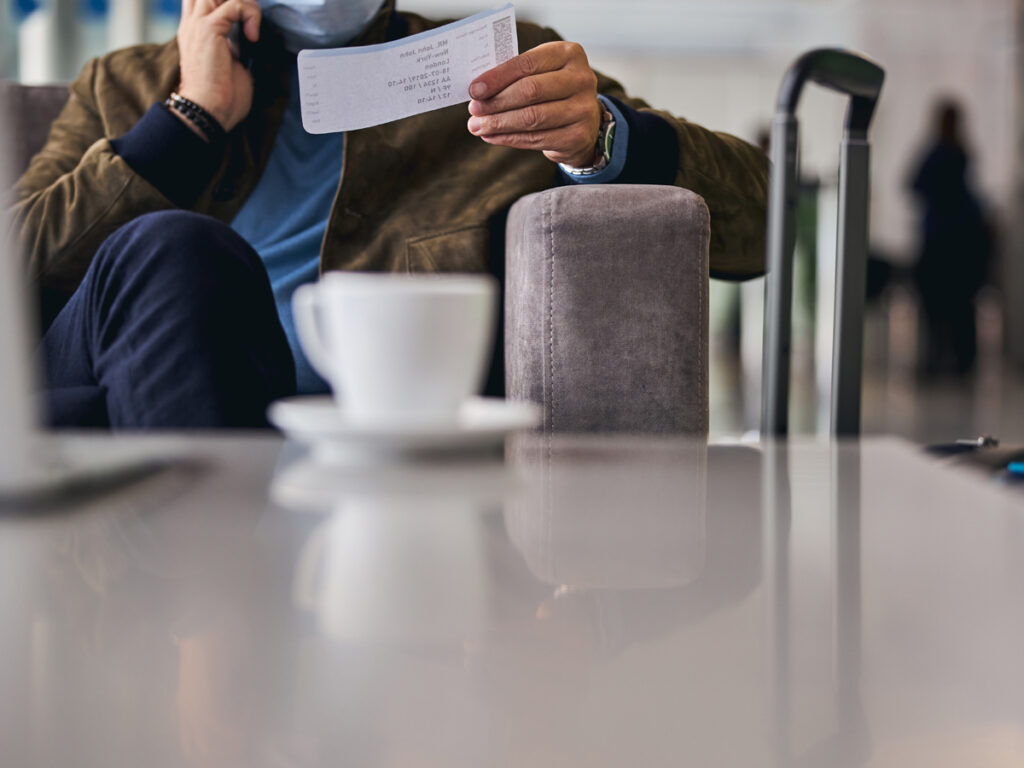 空港のラウンジで搭乗券を手に電話をするビジネスパーソンとテーブルのコーヒーカップ