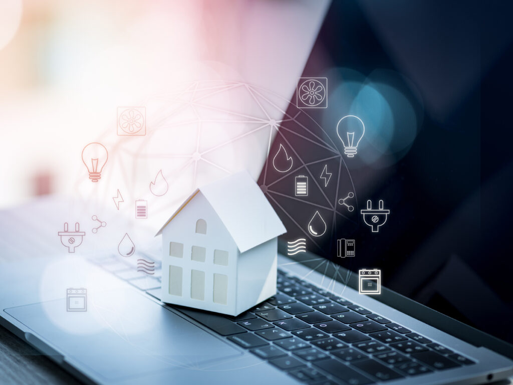 ノートPCの上に置かれた小さな家の模型と、ネットワーク・電気などライフラインのアイコン