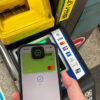 iPhone showing Wise card in Apple Wallet held to a Japan train ticket gate contactless reader with Tap to ride signage.